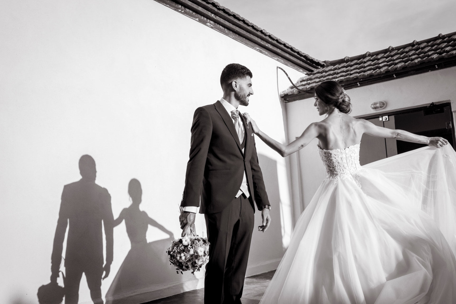 Novios posando juntos en blanco y negro junto a un muro iluminado