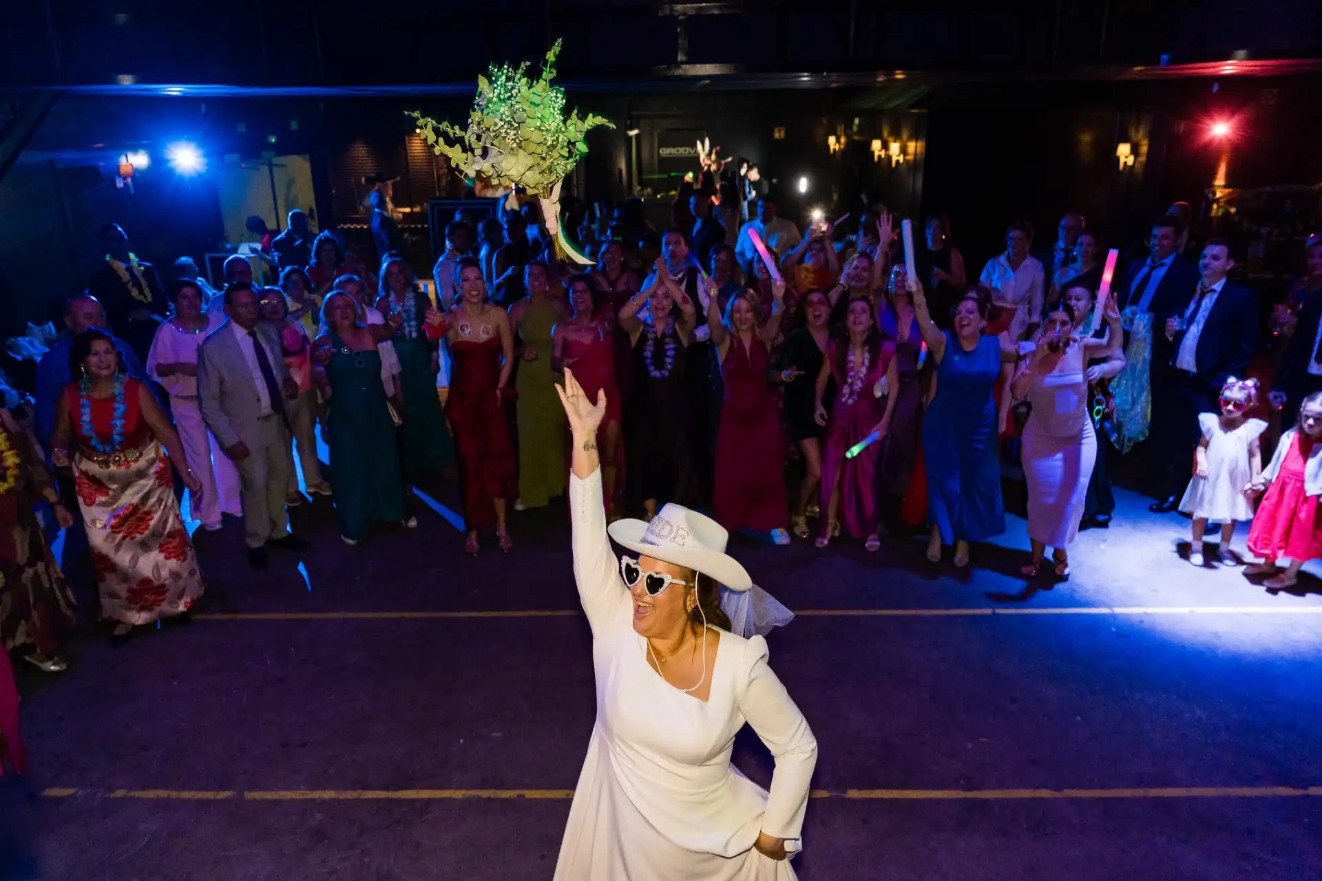 Novia lanzando el ramo de flores entre los invitados en una fiesta de boda con luces de colores