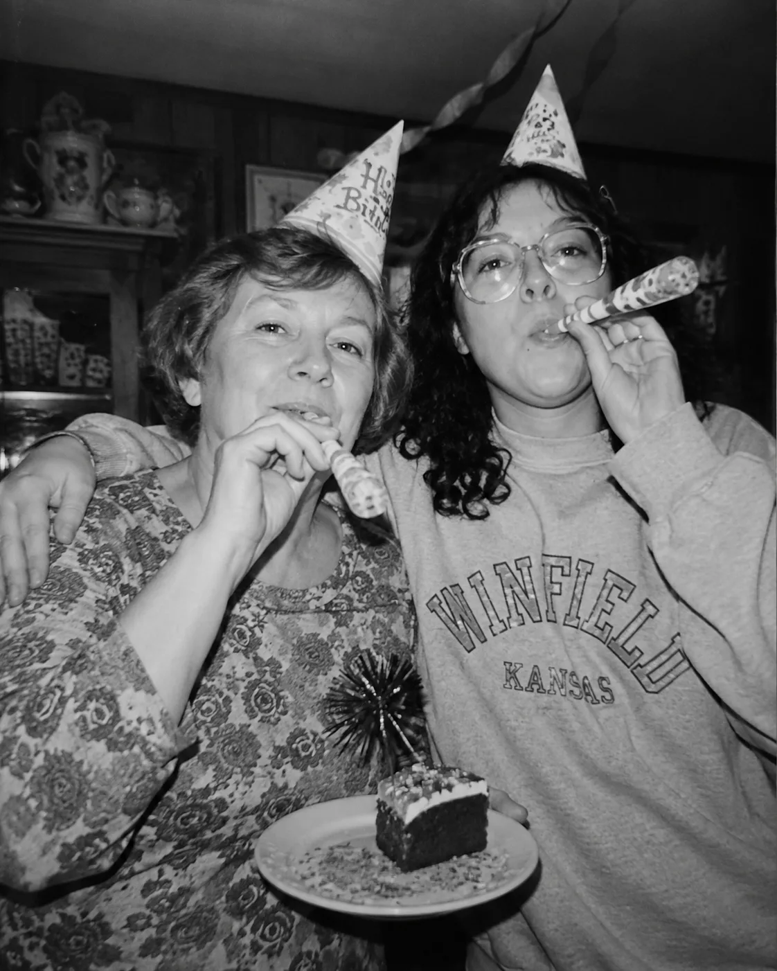 Dos mujeres celebrando con gorros de fiesta y matasuegras