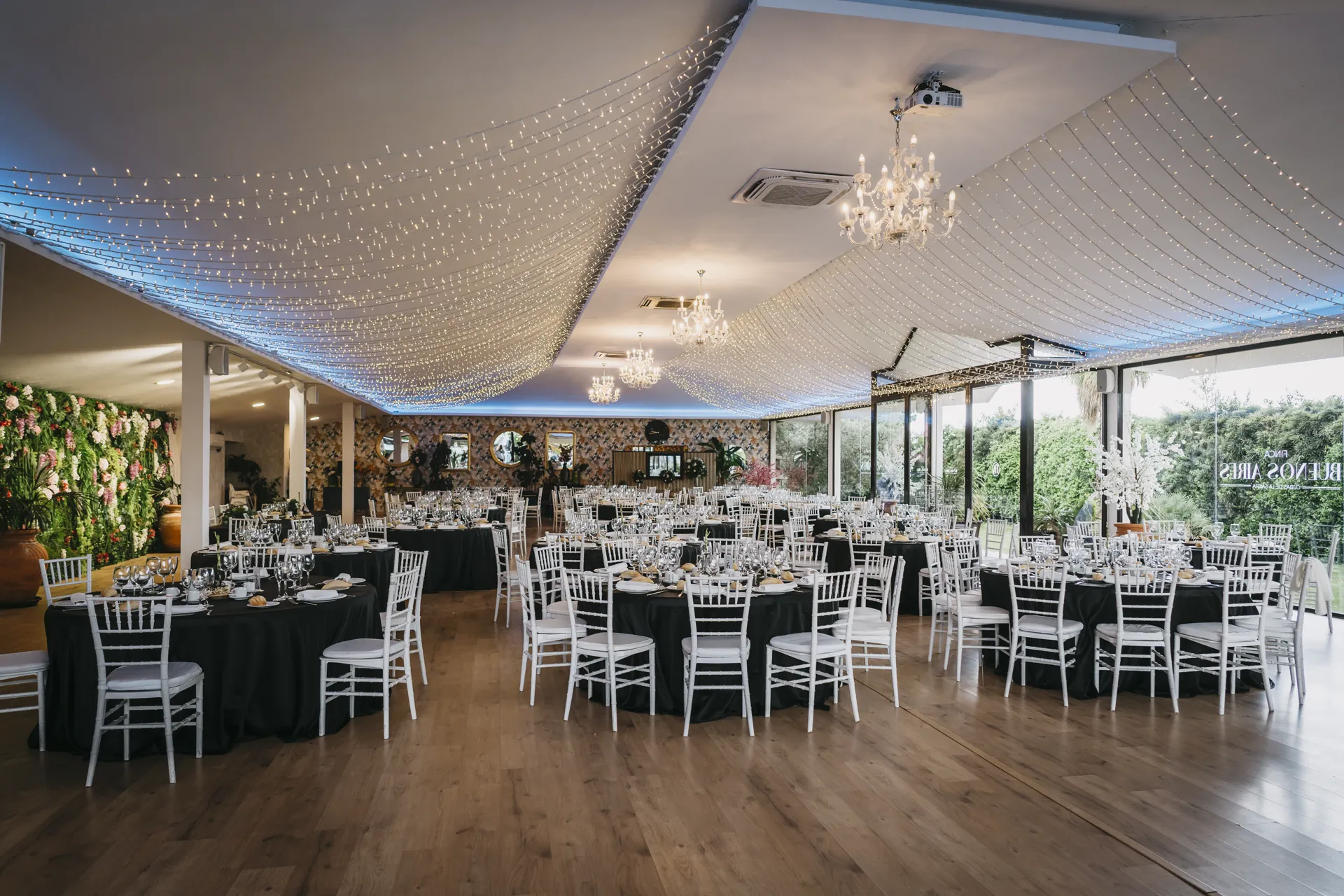 Salón de celebración montado con mesas redondas, lámparas de cristal y guirnaldas de luz