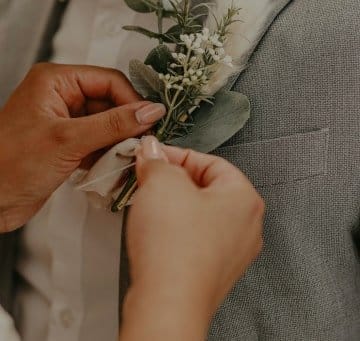 Imagen de una mano colocándole una flor al novio en la chaqueta